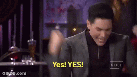 A Man In A Suit And Black Shirt Is Holding His Fist In The Air And Saying Yes . GIF