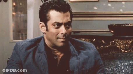 A Man In A Suit And Black Shirt Is Sitting On A Couch And Making A Funny Face . GIF