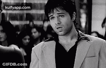 A Man In A Suit And Black Shirt Is Standing In A Crowded Room . GIF