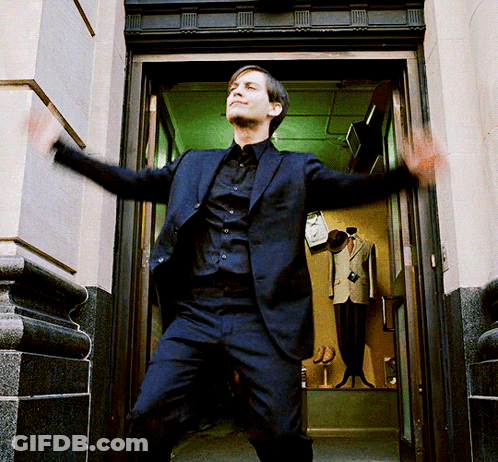 A Man In A Suit And Black Shirt Is Standing In A Doorway With His Arms Outstretched GIF