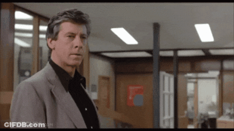 A Man In A Suit And Black Shirt Is Standing In An Office With Movieclips.com On The Bottom Right GIF
