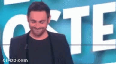 A Man In A Suit And Black Shirt Is Standing In Front Of A Sign That Says `` Cote '' . GIF