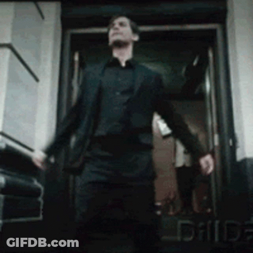 A Man In A Suit And Black Shirt Is Walking Out Of A Door GIF
