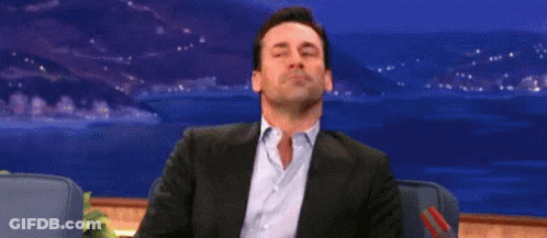 A Man In A Suit And Blue Shirt Is Sitting In A Chair With His Eyes Closed And His Mouth Open . GIF