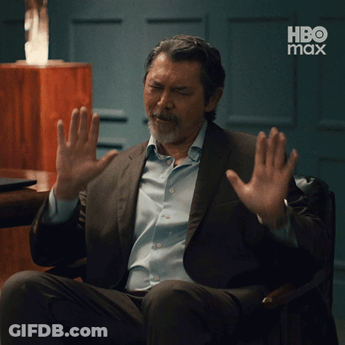 A Man In A Suit And Blue Shirt Is Sitting In A Chair With His Hands Up In Front Of A Hbo Max Logo GIF