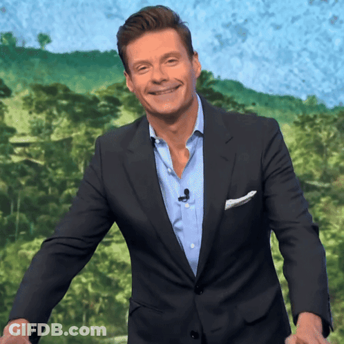 A Man In A Suit And Blue Shirt Is Smiling In Front Of A Green Background GIF