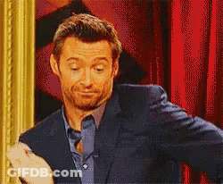 A Man In A Suit And Blue Shirt Is Standing In Front Of A Red Curtain . GIF