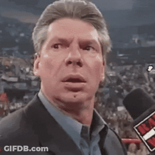 A Man In A Suit And Blue Shirt Is Talking Into A Microphone With A Red T On It GIF
