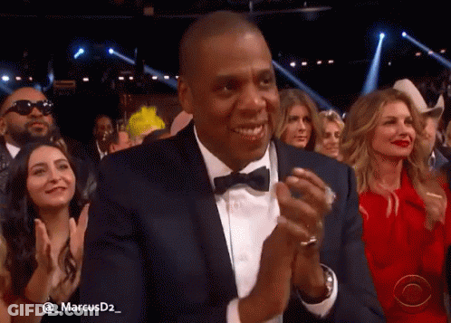 A Man In A Suit And Bow Tie Applauds In A Crowd Of People GIF
