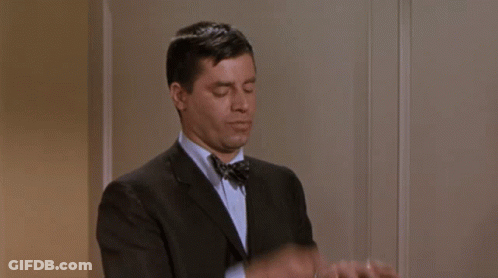A Man In A Suit And Bow Tie Is Adjusting His Cuffs . GIF