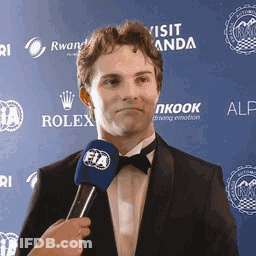 A Man In A Suit And Bow Tie Is Being Interviewed By A Woman Holding A Microphone . GIF