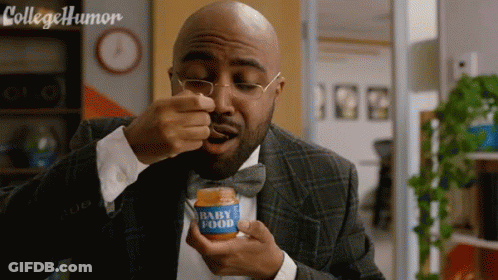 A Man In A Suit And Bow Tie Is Eating From A Jar Of Baby Food GIF