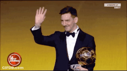 A Man In A Suit And Bow Tie Is Holding A Soccer Ball And Waving . GIF