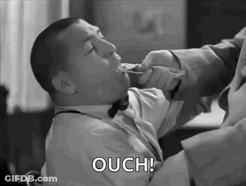 A Man In A Suit And Bow Tie Is Holding A Spoon In His Mouth And Says Ouch . GIF