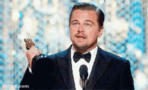 A Man In A Suit And Bow Tie Is Holding A Trophy While Standing In Front Of A Microphone . GIF