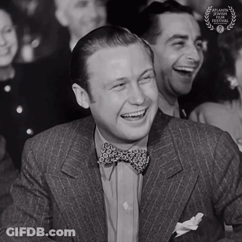 A Man In A Suit And Bow Tie Is Laughing With A Laurel Wreath That Says Atlanta International Film Festival On It GIF