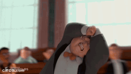 A Man In A Suit And Bow Tie Is Making A Funny Face In A Classroom . GIF