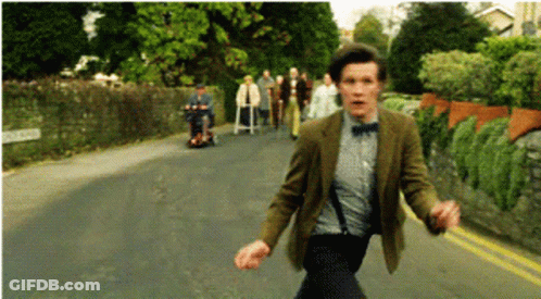 A Man In A Suit And Bow Tie Is Running Down The Street GIF