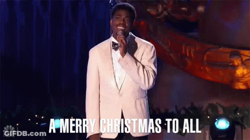 A Man In A Suit And Bow Tie Is Singing Into A Microphone And Saying A Merry Christmas To All . GIF