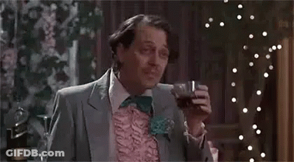 A Man In A Suit And Bow Tie Is Sitting At A Table Holding A Glass Of Wine . GIF