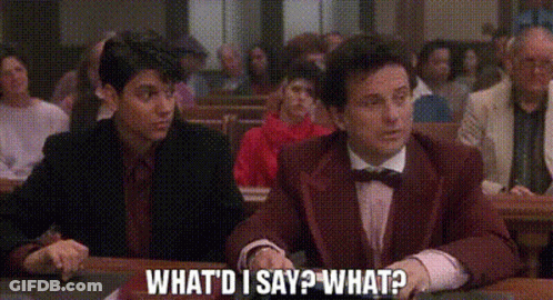 A Man In A Suit And Bow Tie Is Sitting At A Table In Front Of A Crowd Of People . GIF