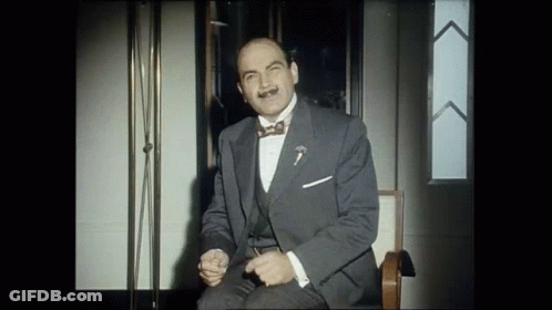 A Man In A Suit And Bow Tie Is Sitting On A Chair GIF