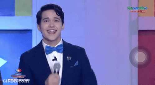 A Man In A Suit And Bow Tie Is Smiling While Standing In Front Of A Microphone . GIF
