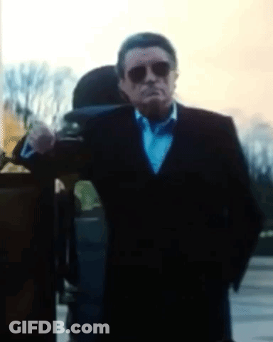 A Man In A Suit And Bow Tie Is Standing In Front Of A Building GIF