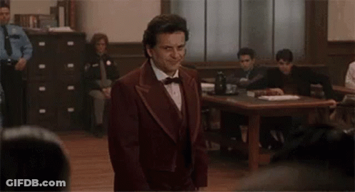 A Man In A Suit And Bow Tie Is Standing In Front Of A Courtroom . GIF