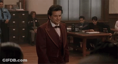A Man In A Suit And Bow Tie Is Standing In Front Of A Courtroom . GIF