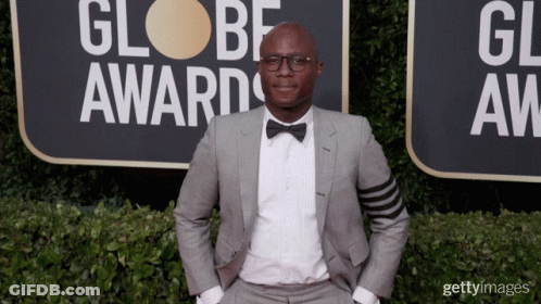 A Man In A Suit And Bow Tie Is Standing In Front Of A Sign That Says Globe Awards GIF