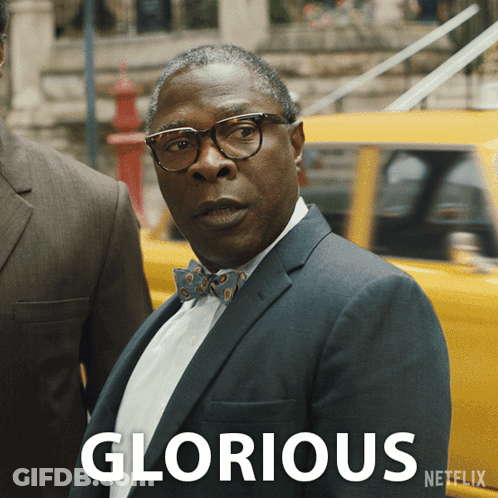 A Man In A Suit And Bow Tie Is Standing In Front Of A Yellow Car With The Word Glorious Written On It GIF