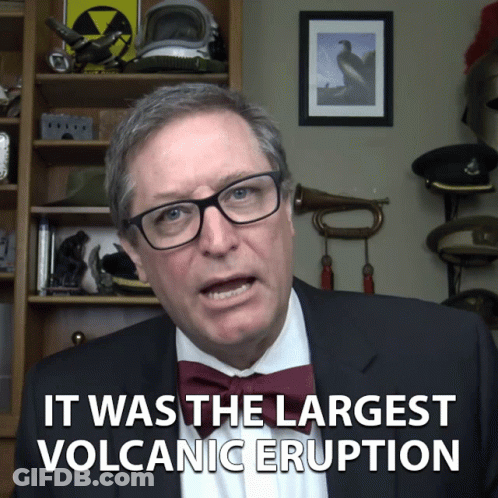 A Man In A Suit And Bow Tie Is Talking About The Largest Volcanic Eruption GIF