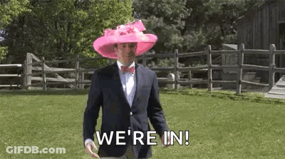 A Man In A Suit And Bow Tie Is Wearing A Pink Hat And Walking In A Field . GIF