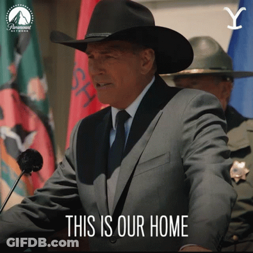 A Man In A Suit And Cowboy Hat Stands At A Podium With The Words " This Is Our Home " Below Him GIF