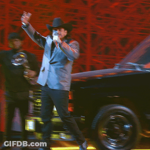 A Man In A Suit And Cowboy Hat Stands On A Stage With His Hand On His Chest GIF