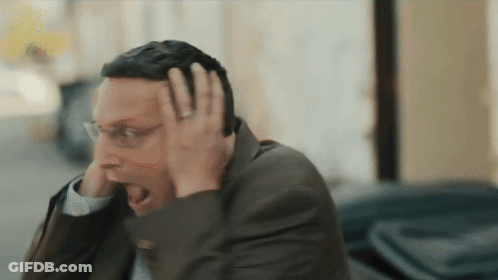 A Man In A Suit And Glasses Is Holding His Head GIF