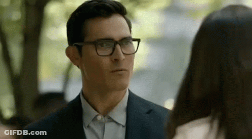 A Man In A Suit And Glasses Is Looking At A Woman In A White Shirt . GIF