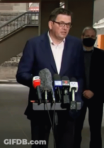 A Man In A Suit And Glasses Is Standing In Front Of A Podium With Microphones . GIF