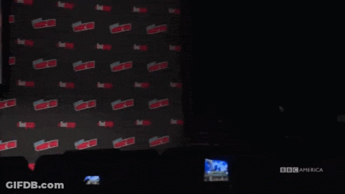 A Man In A Suit And Glasses Is Standing In Front Of A Wall With The Word Expo On It . GIF