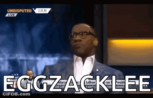 A Man In A Suit And Glasses Says Eggzacklee On A Television Show . GIF