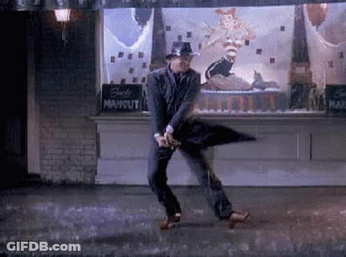 A Man In A Suit And Hat Is Dancing In The Rain With An Umbrella . GIF