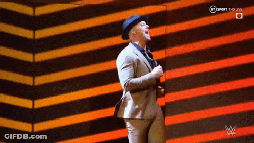 A Man In A Suit And Hat Is Dancing On A Stage In Front Of A Striped Background . GIF