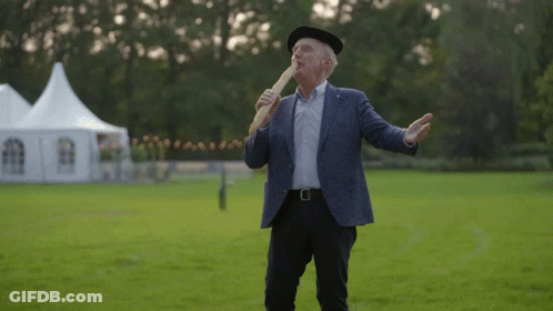 A Man In A Suit And Hat Is Holding A Bread Stick In His Mouth GIF