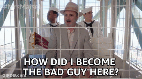A Man In A Suit And Hat Is In A Ferris Wheel Behind Bars And Says How Did I Become The Bad Guy Here GIF