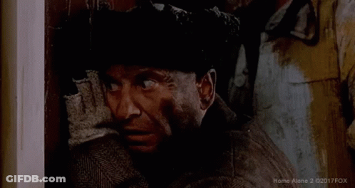 A Man In A Suit And Hat Is Looking Out A Doorway . GIF