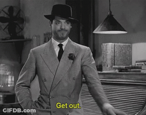 A Man In A Suit And Hat Is Standing In A Room And Says `` Get Out '' . GIF