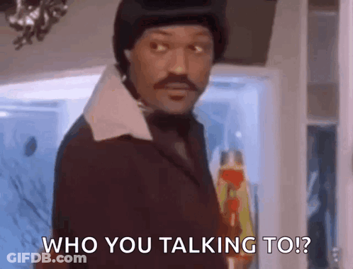 A Man In A Suit And Hat Is Standing In Front Of A Door And Talking To Someone . GIF