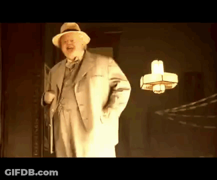 A Man In A Suit And Hat Is Standing In Front Of A Lamp . GIF