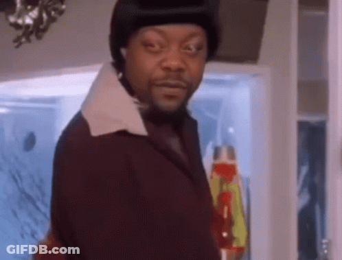 A Man In A Suit And Hat Is Standing In Front Of A Lava Lamp And Looking At The Camera . GIF